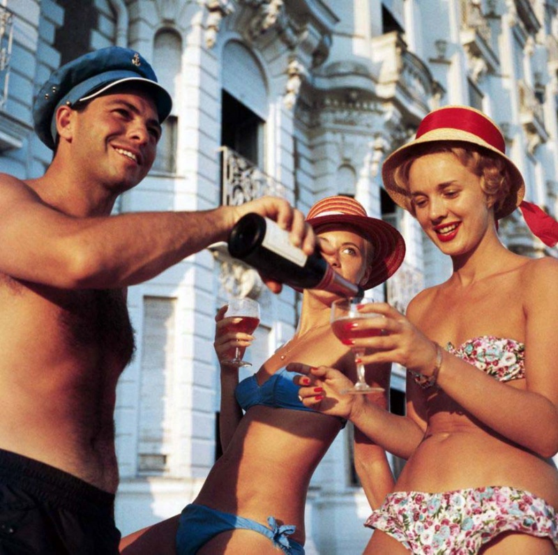<p><b>Slim Aarons</b><i>Sundowners</i>, c. 1958. Two bikini-clad holidaymakers enjoy a glass of wine outside the Carlton Hotel, Cannes. © Slim Aarons</p>