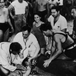 <p><b>Arthur Fellig</b>, <i>Girl smiles on the beach in Coney Island while her boyfriend who just drowned is being tended to by lifeguards</i>, 1940.</p>