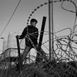 <p><b>James Natchwey</b>, <i>December 2013. Za'atari refugee camp, Jordan. Boys climb the fences to reach the newly arrived refugees and sell them bread, cigarettes and tea.</i></p>