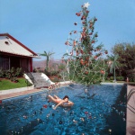 <p><b>Slim Aarons</b>, <i>Christmas Swim</i>, c. 1954. Rita Aarons, wife of photographer Slim Aarons, on a lilo in a swimming pool decorated for Christmas, Hollywood, 1954. The Hollywood sign can be seen in the distance. © Slim Aarons</p>